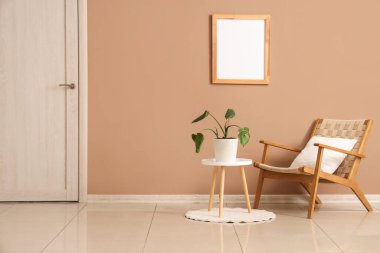 Ev bitkisi, koltuk ve bej duvarın yanındaki fotoğraf çerçeveli şık bir sehpa.