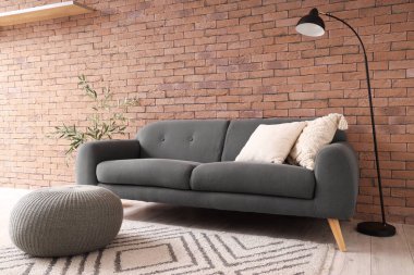 Oturma odasının içinde siyah kanepe, lamba ve puf