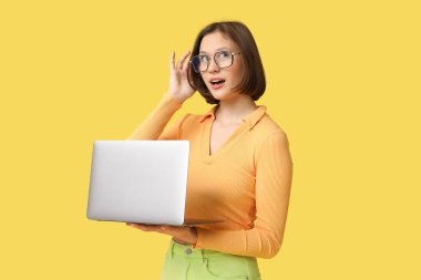 Sarı arka planda modern dizüstü bilgisayarı olan düşünceli genç bir kadın.