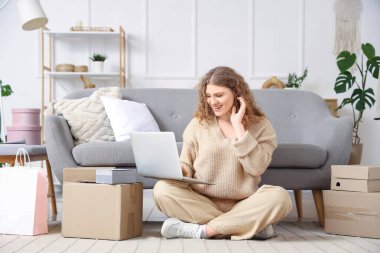 Dizüstü bilgisayarı ve paket kutusu olan genç bir kadın evde online alışveriş yapıyor.