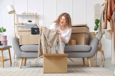 Evde yeni elbisesiyle paket kutusunu açan genç bir kadın.