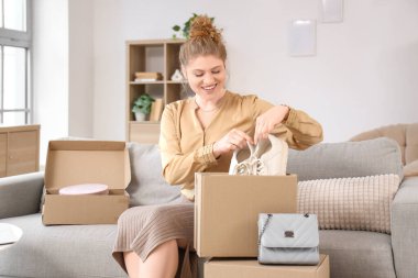 Evdeki kanepede yeni spor ayakkabılarla paket kutusunu açan genç bir kadın.