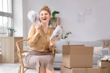 Evde yeni terliklerle paket kutusunu açan genç bir kadın.