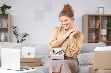 Evde makyaj malzemeleriyle dolu kutuları açan genç bir kadın.