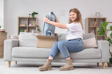 Evdeki kanepede yeni kot ceketli paketleri açan genç bir kadın.