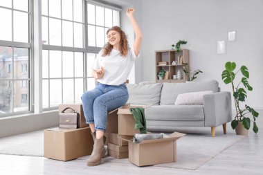 Paket kutularıyla evde oturan mutlu genç kadın.