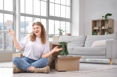 Paket kutularıyla evde oturan genç bir kadın.