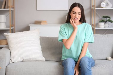 Evdeki kanepede diş ağrısı çeken genç bir kadın.