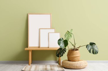 Bankta boş posterler ve odada yeşil duvarın yanında çiçek var.