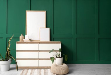 İçinde ev bitkileri ve yeşil duvarın yanında boş posterler olan çekmeceler.