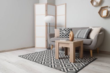 Gri kanepe, lamba ve katlanan ekran ile aydınlık oturma odasının içinde.