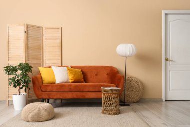 Oturma odasının içinde kırmızı kanepe, lamba ve katlanır ekran var.