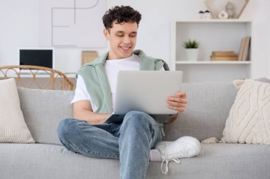 Evdeki kanepede dizüstü bilgisayarla çalışan genç adam.