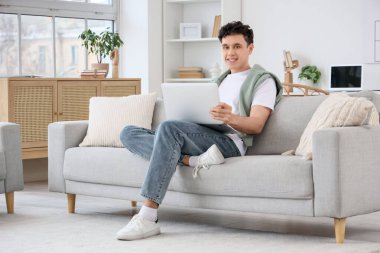 Evdeki kanepede dizüstü bilgisayarla çalışan genç adam.