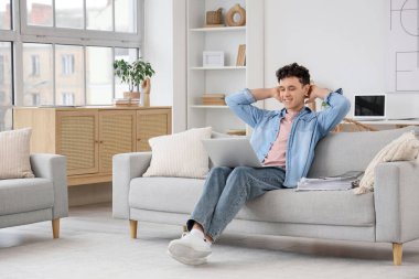 Dizüstü bilgisayarı olan genç adam evdeki kanepede dinleniyor.