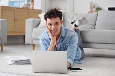 Genç adam evde dizüstü bilgisayarla çalışıyor.