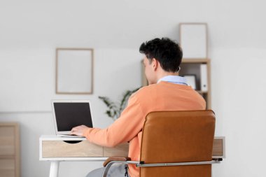 Ofisteki masada dizüstü bilgisayarla çalışan genç bir adam.