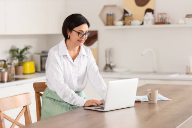 Olgun kadın mutfakta dizüstü bilgisayar kullanarak