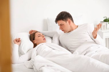 Evde horlayan karısıyla yatakta yatan sinirli genç bir adam.