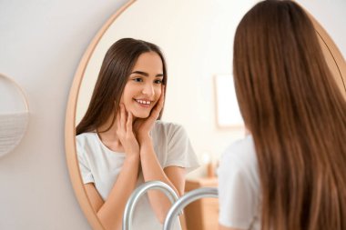 Gülümseyen genç kadın evde aynaya bakıyor