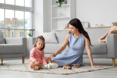 Genç anne ve küçük kızı evdeki halıda tahta oyuncaklarla oynuyorlar.