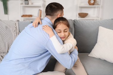 Özür dileyen baba ve kızı evdeki kanepede sarılıyorlar.