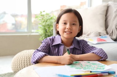 Evdeki masada güzel bir Asyalı kız çiziyor.