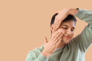 Genç adam bej arka plan üzerinde yüz geliştirme egzersizi yapıyor.