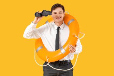 Kurtarma yüzüğü ve sarı arka planda dürbünü olan genç bir iş adamı.