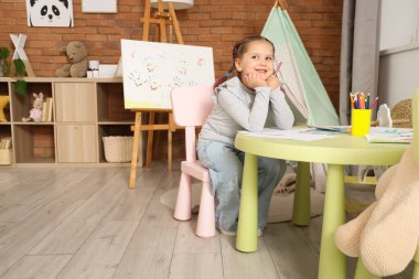 Evdeki masada kalem çizen düşünceli küçük kız.