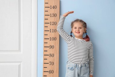 Evdeki mavi duvarın yanında küçük bir kız stadyum ölçer ile boy ölçüyordu.