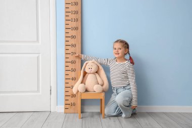 Evdeki stadyumun yanındaki sandalyede boyunu ölçen küçük kız.