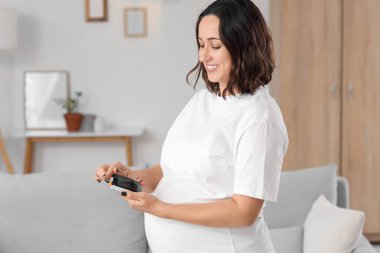 Genç hamile kadın evde glukometre kullanıyor. Gebelik Diyabet Konsepti