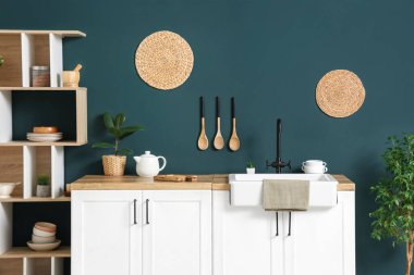 Mutfağın içinde raf ünitesi ve mavi duvarın yanında beyaz tezgahlar var.