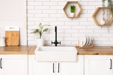 Mutfaktaki beyaz tuğla duvarın yanında lavabo ve çiçek tezgahları var.