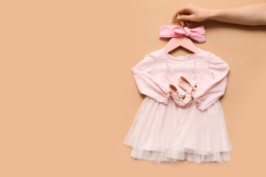 Şık bir bebek elbisesi, patik ve saç bandı olan kadın eli.