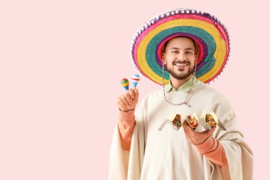 Pembe arka planda lezzetli tacoları ve marakaları olan genç Meksikalı adam.