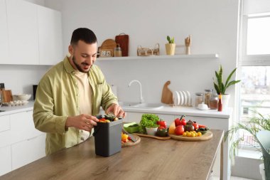 Mutfakta yemek pişirirken gübre kutusu ve sebze artıklarıyla gezen genç adam.