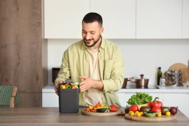Mutfakta yemek pişirirken gübre kutusu ve sebze artıklarıyla gezen genç adam.