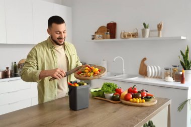 Mutfakta yemek pişirirken gübre kutusu ve sebze artıklarıyla gezen genç adam.