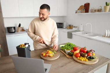 Mutfakta yemek pişirirken dizüstü bilgisayarı, gübre kutusu ve sebze artıkları olan genç bir adam.