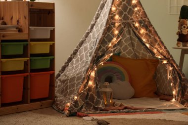 Şık çocukların yatak odasının içinde oyun çadırı, parlayan ışıklar ve gece oyuncakları var.