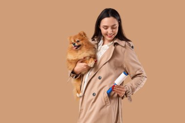 Paltolu genç bir kadın, kahverengi arka planda pamuklu silindir ve tüylü bir köpek
