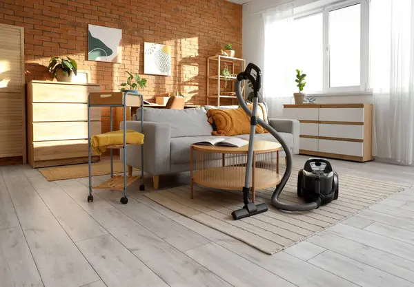 Oturma odasının içinde elektrikli süpürge, kanepe ve masa var.