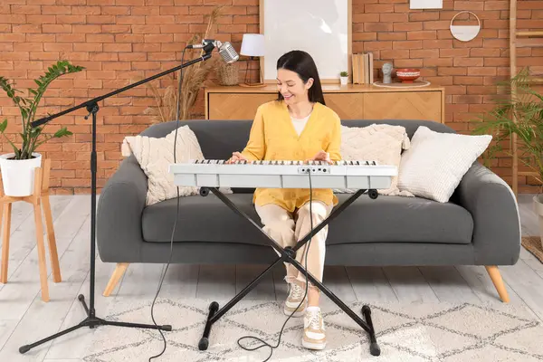 Mutlu genç bir kadın evdeki kanepede sentezleyici oynuyor.