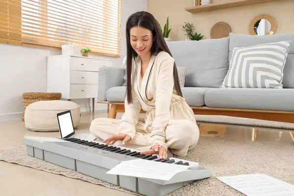 Evde pijamalı genç bir kadın halı üzerinde sentezleyici oynuyor.