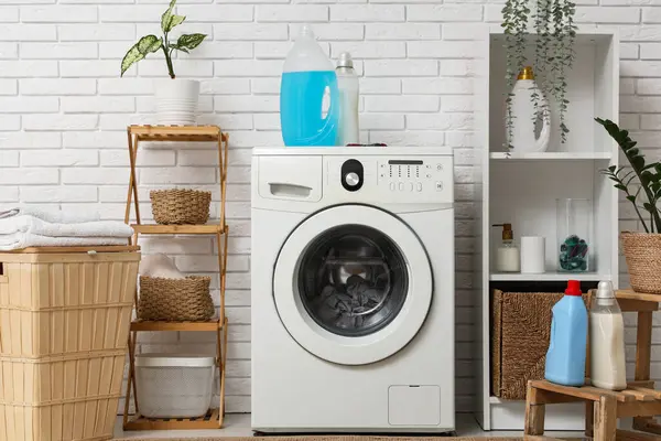 Çamaşırhane içi çamaşır makinesi, sepet ve deterjan dolu.