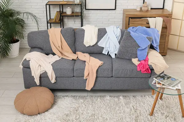 Gri kanepesi, kahve masası ve dağınık giysileri olan dağınık bir oturma odası.