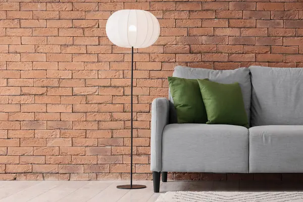 Yastıklı gri kanepe ve tuğla duvarın yanında parlayan lamba.