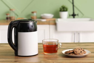 Mutfaktaki ahşap masada cam çay ve tatlı kurabiyeli modern elektrikli çaydanlık.